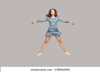 Full length girl vintage ruffle dress levitating hovering in mid-air, spread hands legs like a star, jumping trampoline, flying up and looking at camera. indoor studio shot isolated on gray background