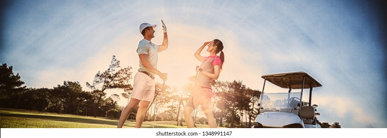 Full length of golf player couple giving high five while standing on field - Powered by Shutterstock