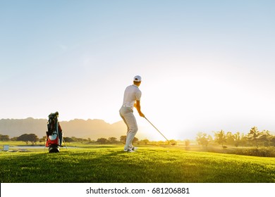 Full length of golf player playing golf on sunny day. Professional male golfer taking shot on golf course. - Powered by Shutterstock