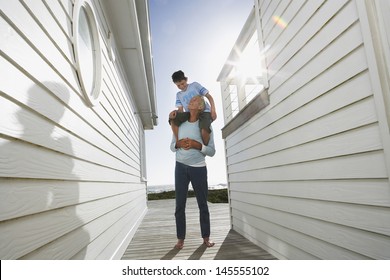 Full length of grandfather carrying grandson on shoulders between beach houses