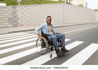 Full length of handicapped black man in wheelchair crossing street, using crosswalk outdoors. Impaired young guy going for walk alone in urban district. Living well with disability concept - Powered by Shutterstock