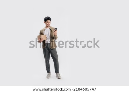 Full length handsome Asian man holding box and use smartphone on isolated white background. Cool man cheerful using mobile phone with shopping online concept.