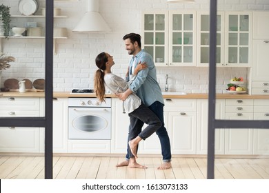 Full Length Handsome Young Man Embracing And Dropping Smiling Mixed Race Wife During Passionate Romantic Dance In Kitchen. Happy Family Couple Having Fun, Dancing Together Barefoot On Wooden Floor.