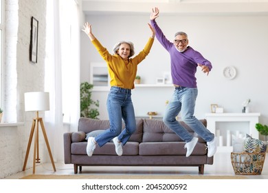 Full length of happy active energetic senior caucasian family couple jumping and having fun together in living room at home, looking at camera and smiling, retired people enjoying life on retirement