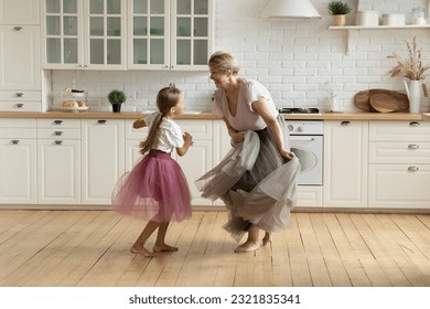 Full length happy barefoot 7s cute little kid girl and older retired grandmother wearing puffy skirts, dancing together in modern kitchen, active different generations family playing on weekend. - Powered by Shutterstock