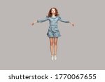 Full length happy calm pretty girl in vintage ruffle dress levitating hovering in mid-air with raised hands as wings, jumping trampoline or flying up. indoor studio shot isolated on gray background