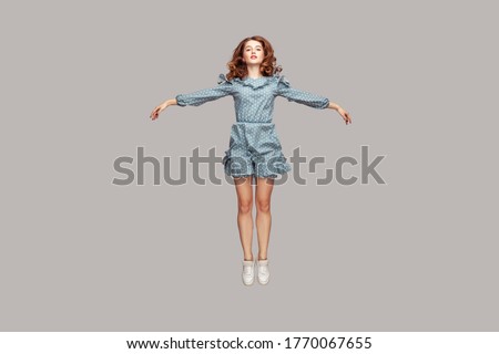 Full length happy calm pretty girl in vintage ruffle dress levitating hovering in mid-air with raised hands as wings, jumping trampoline or flying up. indoor studio shot isolated on gray background