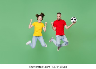 Full Length Of Happy Couple Friends Sport Family Woman Man Football Fans In T-shirts Cheer Up Support Favorite Team With Soccer Ball Jumping Doing Winner Gesture Isolated On Green Background Studio