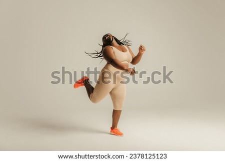 Full length of happy curvy African woman in sportswear dancing on studio background