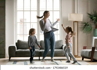 Full Length Happy Energetic Young Mother Dancing To Disco Music With Overjoyed Little Children Siblings In Living Room At Home. Joyful Mum With Small Daughter And Son Involved In Funny Activity.