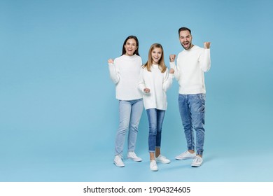 Full Length Of Happy Joyful Young Parents Mom Dad With Child Kid Daughter Teen Girl In White Sweaters Doing Winner Gesture Isolated On Blue Background Studio Portrait. Family Day Parenthood Concept