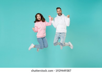 Full length happy joyful young couple friends man woman in white pink casual hoodie jumping doing winner gesture clenching fists looking camera isolated on blue turquoise background studio portrait