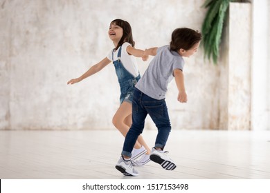 Full Length Happy Little Boy And Girl Holding Hands, Twisting, Running, Playing Together, Laughing. Energetic Excited Siblings Having Fun At Home, Engaged In Indoors Activity, Feeling Overjoyed.