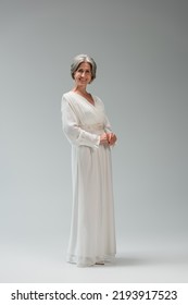 Full Length Of Happy Middle Aged Bride In White Wedding Dress Standing On Grey