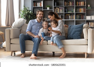 Full Length Happy Millennial Parents Cuddling Adorable Little Children, Posing For Selfie Photo On Smartphone. Joyful Different Generations Family Recording Funny Video On Mobile Phone At Home.