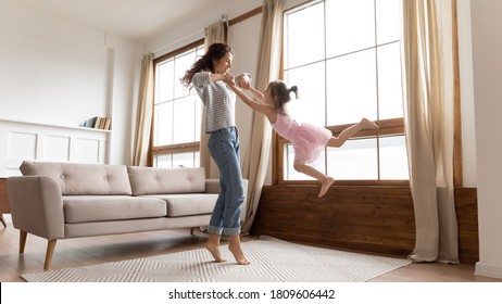 Full length happy mother holds hands spinning carefree adorable little daughter listen music moving in modern interior light cozy living room. Active funny games, lively play have fun together at home