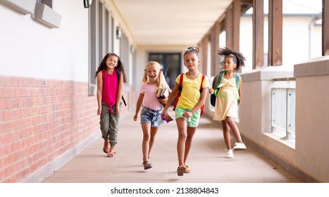 Full length of happy multiracial elementary schoolgirls walking in corridor. unaltered, childhood, together, education and back to school concept. - Shutterstock ID 2138804843
