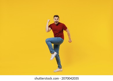 Full length happy overjoyed excited caucasian young man 20s wear red t-shirt casual clothes doing winner gesture clench fist celebrating isolated on plain yellow color wall background studio portrait.