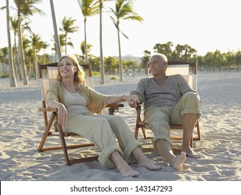Full length of happy senior couple relaxing on deckchairs at tropical beach