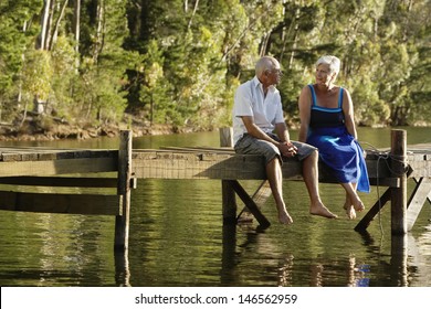 Full length of happy senior couple sitting on pier at lake