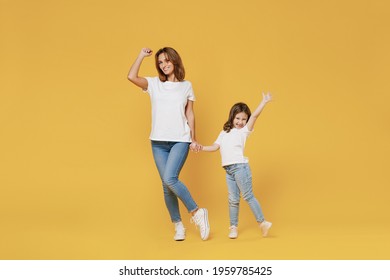 Full Length Happy Woman In Basic White T-shirt Have Fun With Cute Child Baby Girl 5-6 Years Old Hold Hands. Mom Little Kid Daughter Isolated On Yellow Color Background Studio. Mother's Day Love Family