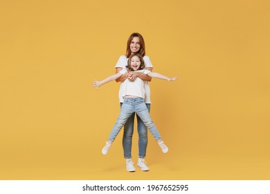 Full Length Happy Woman In Basic White T-shirt Have Fun Hold On Hands Cute Child Baby Girl 5-6 Years Old. Mom Little Kid Daughter Isolated On Yellow Color Background Studio. Mother's Day Love Family