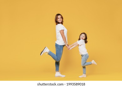 Full Length Happy Woman In Basic White T-shirt Have Fun With Cute Child Baby Girl 5-6 Years Old Hold Hands. Mom Little Kid Daughter Isolated On Yellow Color Background Studio. Mother's Day Love Family