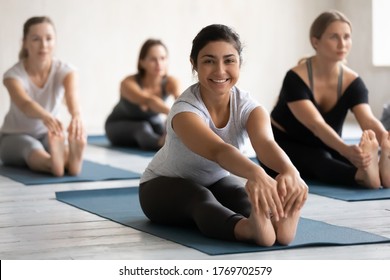 Full length happy young sporty active indian ethnicity woman sitting in seated forward bend position, looking at camera. Smiling millennial biracial female yoga beginner enjoying exercises at class. - Powered by Shutterstock