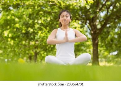 Full length of healthy and beautiful young woman sitting with joined hands at park
