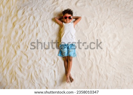 Full length high angle view photo of cheerful cute little boy wear white shirt dark spectacles lying arms behind head outside sea beach