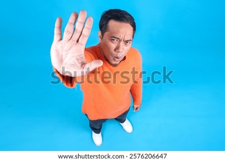 Full Length High Angle View Of Young Man Saying No Gesture Rejection To Camera On Blue Studio Wall 