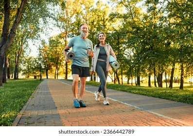 Full length image of beautiful sporty healthy active cheerful middle age couple going to exercise outdoors in park holding mats for yoga, pilates, gym. Sports healthy lifestyle. Loving older couple.
 - Powered by Shutterstock