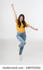 Full length image of excited brunette woman wearing casual clothes laughing and rejoicing with arms raised isolated over white background