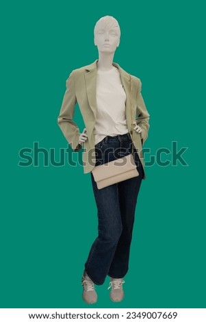 Full length image of a female display mannequin wearing fashionable yellow jacket and blue jeans isolated on green background