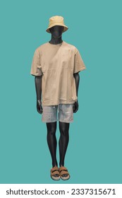 Full length image of a male display mannequin wearing beige t-shirt gray shorts and hat isolated on a green background 