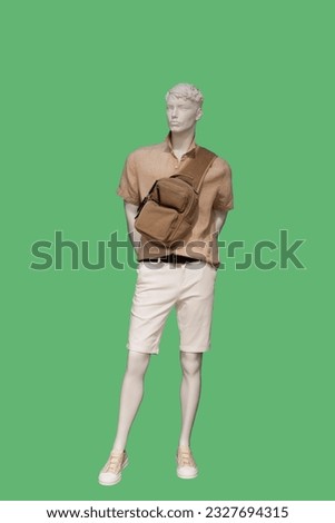 Full length image of a male display mannequin wearing short sleeve button down brown shirt and white shorts with sling bag. Isolated on green background 