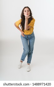 Full length image of pretty brunette woman wearing casual clothes blowing air kiss at camera isolated over white background