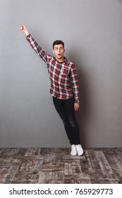 Full Length Image Of Surprised Man In Shirt And Jeans Holding Copyspace In Hand And Looking At The Camera Over Gray Background