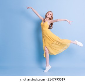 Full length image of young Asian woman wearing yellow dress on blue background - Shutterstock ID 2147993519