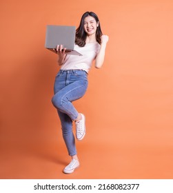 Full Length Image Of Young Asian Girl Using Laptop On Orange Background