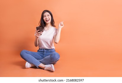 Full length image of young Asian girl using smartphone on orange background