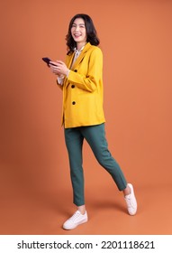 Full length image of young Asian woman using smartphone on background