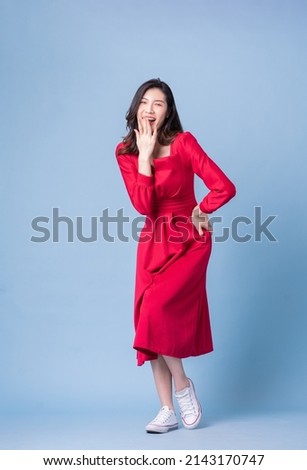 Full length image of young Asian woman wearing red dress on blue background