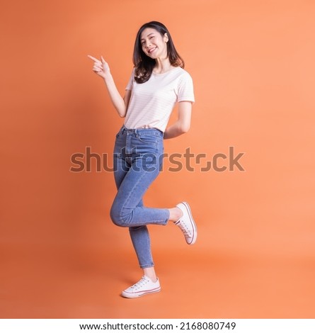 Full length image of young Asian woman posing on orange background