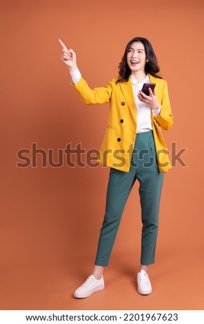 Full length image of young Asian woman using smartphone on background