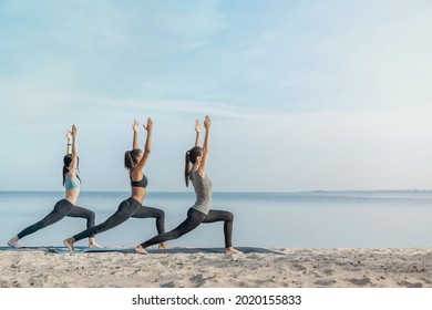 Full Length Image Of Young Multiethnic Group Of Woman Practicing Yoga Exercise At The Beach Near Water. Stretching Exercises, Active Lifestyle, Fitness, Pilates, Workout Outdoors.