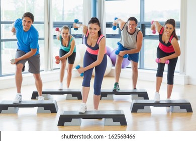 Full length of instructor with fitness class performing step aerobics exercise with dumbbells in a gym - Powered by Shutterstock