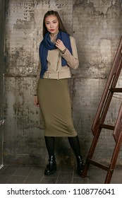 Full length isolated studio portrait of a young Asian lady in an olive skirt, a beige jacket and a navy blue scarf. The brunette girl posing over the grunge rusty background, looking at the camera.