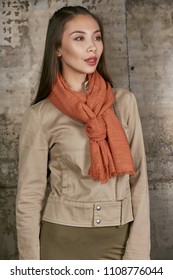 Full length isolated studio portrait of a young Asian lady in an olive skirt, a beige jacket and a black scarf. The brunette girl posing against the grunge rusty background, looking at the camera.
