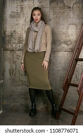 Full length isolated studio portrait of a young Asian lady in an olive skirt, a beige jacket and a grey scarf. The brunette girl posing over the grunge rusty background, looking at the camera.